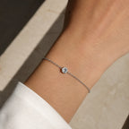 Bracelet SAONA en or blanc 18 carats avec diamant rond de laboratoire porté au poignet d'une femme en chemise blanche
